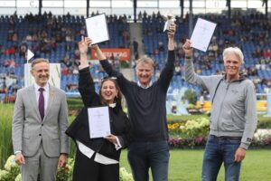 Four people are presenting their awards at a ceremony in the Main Stadium. A woman and two men are holding up framed certificates bearing the words ‘Silver Camera’, whilst another man is presenting a trophy. In the background, spectators are seated in the stands.